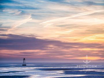 Das Unterfeuer vor Pellworm bei Ebbe. Orange, violett und purpur verfärbt sich der Himmel im Sonnenuntergang. Ein Fotomotiv, das Sehnsucht nach der Insel weckt.