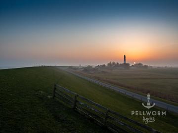 Der Leuchtturm von Pellworm im winterlichen Sonnenuntergang unter einem wolkenlosen Himmel. Von leichtem Dunst und Bodennebel umgeben.